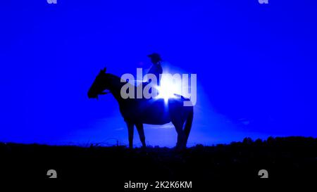 Silhouette de cowgirl à cheval au coucher du soleil en bleu Banque D'Images