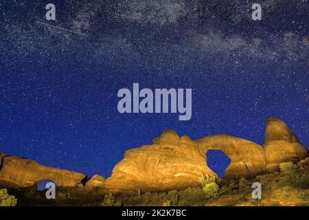 The Milky Way Galaxy & meteorite over Turret Arch & North Window in Arches National Park near Moab, Utah, USA.  A small spotlight was used to light pa Stock Photo