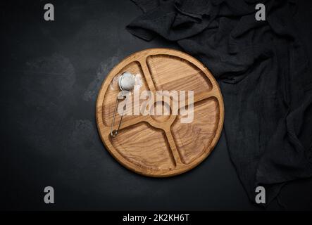 plateau rond en bois pour servir de la nourriture et un tamis avec du sucre sur une table noire, vue du dessus Banque D'Images