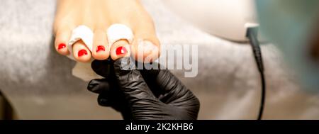 Processus de peinture des ongles. Une main maîtresse de manucure tient les ongles peints en rouge sur une jambe femelle dans un salon de beauté Banque D'Images