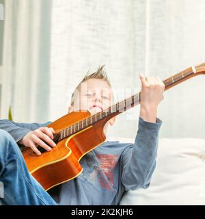 Musique jeune garçon strummin sur une guitare à la maison Banque D'Images