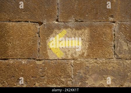 La flèche jaune peinte sur un mur en pierre indique la direction du pèlerinage à Saint-Jacques-de-Compostelle Banque D'Images