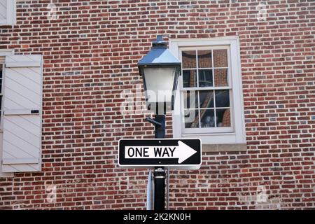 Affiche à sens unique accrochée à un poteau noir avec une lampe de rue, avec un mur traditionnel en brique à l'arrière Banque D'Images