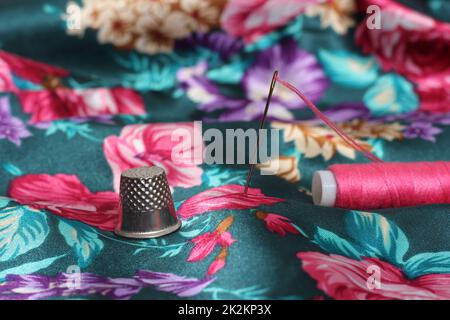 Filet avec aiguille et fil rose sur tissu satiné à motif fleuri d'époque Banque D'Images