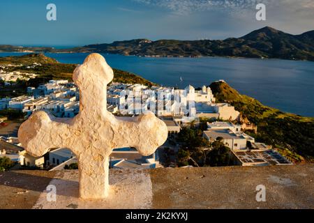 Croix chrétienne et village de Plaka sur l'île de Milos sur rouge Géranium fleurs au coucher du soleil en Grèce Banque D'Images