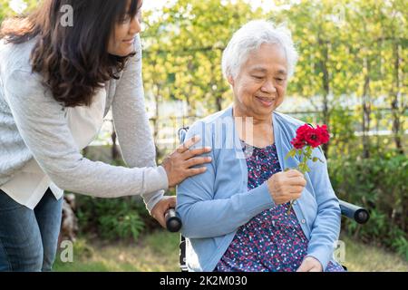 La fille du soignant se câlin et aide la vieille femme asiatique âgée ou âgée qui tient une rose rouge sur un fauteuil roulant dans le parc. Banque D'Images