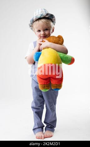 petit bébé avec chapeau qui embrasse son ours en peluche Banque D'Images