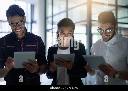 Synchronisation de leurs appareils et réussite.Prise de vue de trois collègues utilisant des tablettes numériques dans un bureau. Banque D'Images