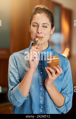 Savourer une cuillerée de joie. Dose de culture d'une jeune femme mangeant du beurre d'arachide dans le pot avec une cuillère. Banque D'Images