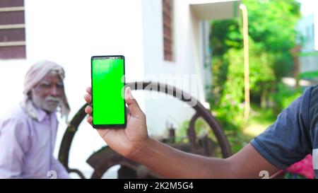 Jeune homme asiatique montrant un téléphone cellulaire à écran vert avec fond de concept de vie de village rural. Banque D'Images