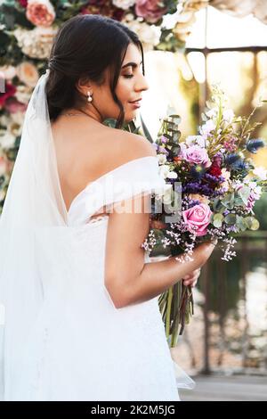 Je suis la plus heureuse fille du monde aujourd'hui. Photo d'une jeune mariée heureuse et belle tenant son bouquet de fleurs tout en posant à l'extérieur le jour de son mariage. Banque D'Images