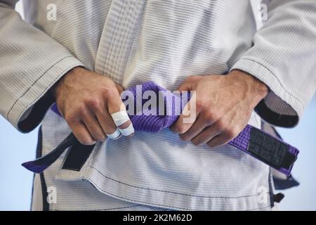 HES un professionnel chevronné. Coupe courte d'un homme méconnaissable nouant une ceinture mauve autour de la taille du poing tout en jiu jitsu gi complet. Banque D'Images