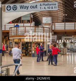Un équipage de gare se trouve dans un groupe qui parle sur un hall. Un kiosque et une passerelle sont en arrière-plan. Un toit historique incurvé est en hauteur. Banque D'Images