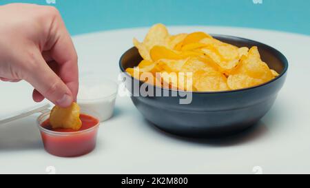 vue partielle de l'homme qui coupe des chips de pommes de terre striées dans le ketchup sur image bleue, stock Banque D'Images