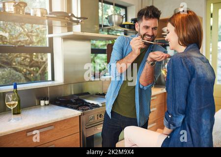 La nourriture a un meilleur goût quand elle est faite avec amour. Photo d'un homme donnant à sa femme un goût de la nourriture qui se prépare à la maison. Banque D'Images