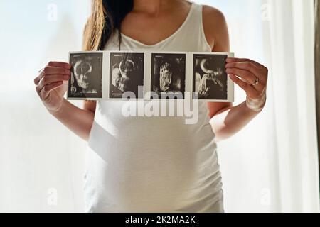 Premier portrait de Babys. Prise de vue d'une femme enceinte non identifiable tenant une série d'images échographiques devant une fenêtre à la maison. Banque D'Images