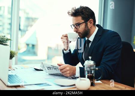 Voyons comment les marchés se portent. Photo d'un jeune homme d'affaires qui boit une tasse de thé tout en lisant un journal dans un bureau. Banque D'Images