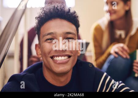 La vie universitaire est grande. Portrait court d'un jeune étudiant de sexe masculin assis sur un escalier de campus avec ses amis. Banque D'Images