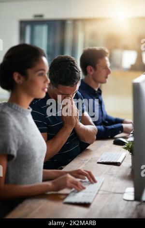 Ses collègues seront également malades avec ses éternuements sans arrêt. Photo d'un jeune homme d'affaires qui soufflait le nez tout en travaillant aux côtés de ses collègues dans un bureau. Banque D'Images