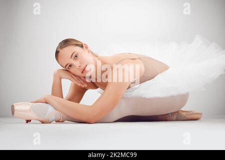 Mon but est de impressionner le public. Portrait d'une jeune danseuse de ballet attirante en studio sur fond gris. Banque D'Images