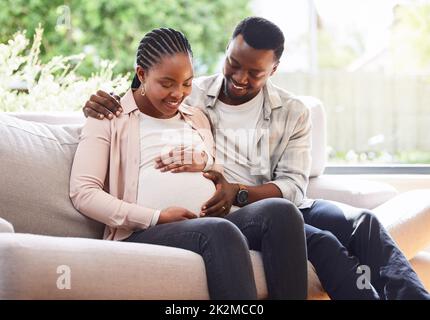 Avez-vous ressenti une sensation. Photo courte d'un jeune couple affectueux de parents assis sur le canapé à la maison. Banque D'Images