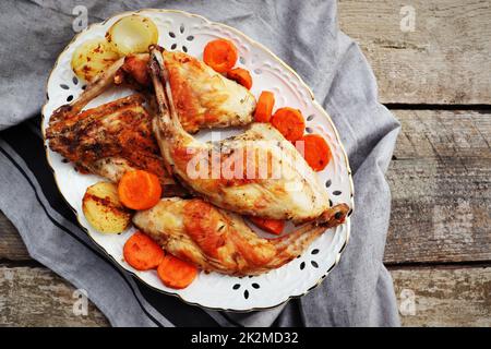 Des haunches de lapin grillées sur une assiette blanche avec des légumes cuits sur une surface de table en bois rustique Banque D'Images