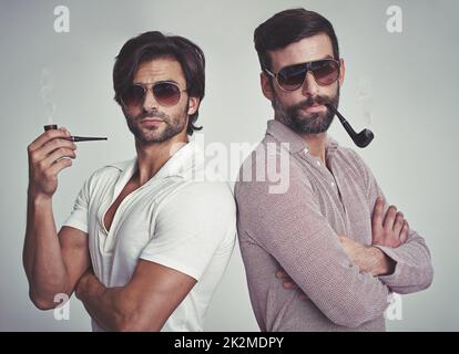 Ils ont beaucoup de style.Photo de studio de deux hommes debout ensemble tout en portant des tuyaux d'usure rétro 70s et de fumée. Banque D'Images