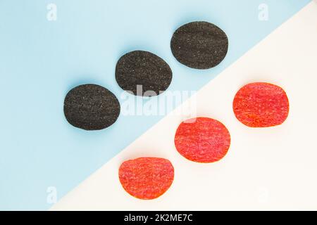 Chips de pommes de terre rouges et noires avec sel, piment. Mise en plan isométrique. Fond de puce sur fond blanc et bleu. Banque D'Images