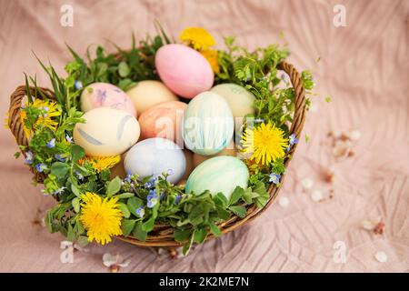 Sur un pastel couvrir un panier avec des herbes et des fleurs brillantes. Le panier contient des œufs de Pâques peints en aquarelle dans de belles couleurs pastel. Super Pâques. Banque D'Images