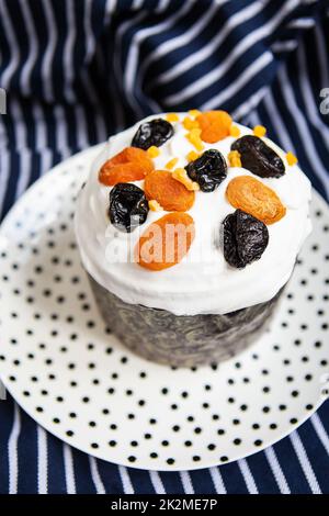 Un gâteau de Pâques décoré d'abricots et de pruneaux séchés se dresse sur une assiette et un tablier bleu rayé. Concept de vacances religieuses de Pâques. Banque D'Images