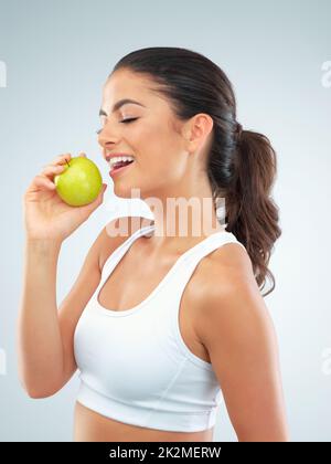 Corps sain, coeur heureux. Photo studio d'une jeune femme en forme mangeant une pomme sur fond gris. Banque D'Images