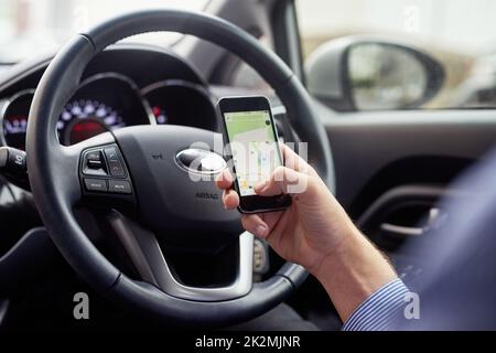 Laissez votre GPS vous guider. Gros plan d'un conducteur dans une voiture à l'aide d'un téléphone portable pour trouver un itinéraire. Banque D'Images