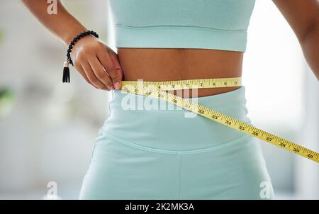 Quelques pouces de plus et ID ont atteint mon objectif. Plan court d'une femme non reconnaissable debout seule et utilisant un mètre ruban autour de sa taille dans un studio de yoga. Banque D'Images