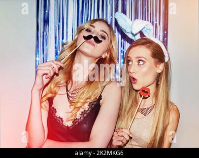 Étaient la vie de la partie. Photo de deux jeunes femmes qui s'amusent avec des accessoires dans un photomasque. Banque D'Images