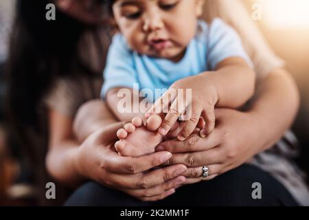 Ce petit porcin rentrait à la maison. Gros plan d'une femme méconnue qui tient ses enfants les pieds tout en étant assise sur un canapé à la maison pendant la journée. Banque D'Images