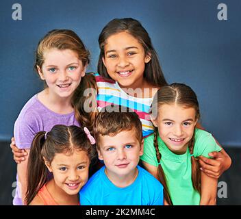 L'amitié compte. Photo en studio d'un groupe varié d'enfants se posant ensemble sur un fond bleu. Banque D'Images