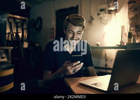 Rester connecté et à jour. Photo rognée d'un beau jeune homme envoyant un texte tout en travaillant tard dans son bureau. Banque D'Images