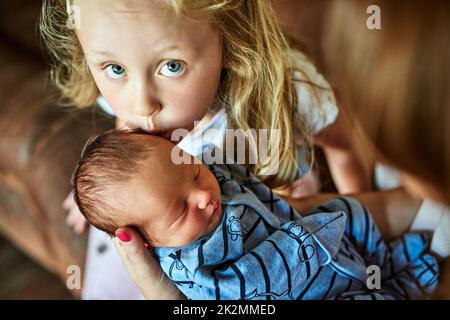 Grande sœur montrant son amour. Photo d'une petite fille affectueuse et gaieuse donnant à son petit frère un baiser dans le front tout en regardant l'appareil photo à la maison. Banque D'Images