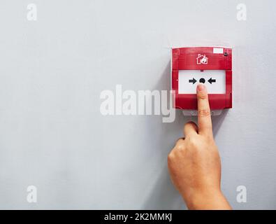 Activation de l'alarme. Photo rognée d'une personne appuyant sur une alarme incendie sur un mur. Banque D'Images