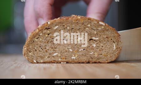 Trancher du pain à grains entiers sur une table en bois. Banque D'Images