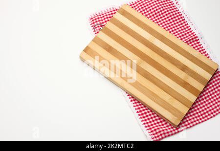 une planche à découper rectangulaire en bois vide et une serviette rouge dans une cage blanche sur une table blanche, vue du dessus Banque D'Images