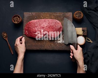 Le filet de bœuf cru se trouve sur une planche à découper en bois et des épices pour cuisiner sur une table noire, vue du dessus Banque D'Images