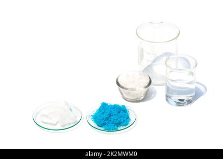 Cristal d'alun et sulfate de cuivre(II) dans le Chemical Watch Glass sur une table de laboratoire blanche. Le sel de flocons dans un contenant en verre et l'alcool dans un bécher ont été placés en arrière-plan. Banque D'Images