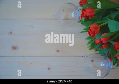 Des tulipes roses aux feuilles vertes se trouvent dans le coin supérieur sur fond de bois, et des verres à vin se trouvent sur les côtés du bouquet Banque D'Images