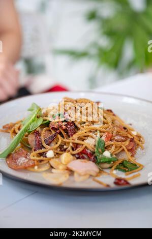 Spaghetti au bacon, à l'ail, au basilic et au fromage dans une assiette blanche Banque D'Images