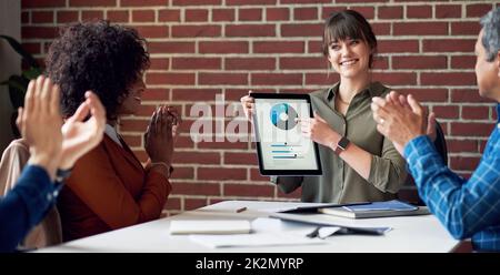 une femme d'affaires heureuse utilisant une tablette numérique pour présenter des données financières à l'écran avec des collègues qui claque les mains pour féliciter le succès Banque D'Images