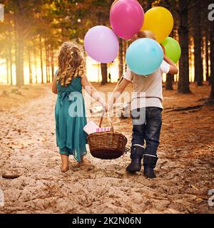 Les meilleurs amis se collent ensemble. Photo d'un petit garçon et d'une fille méconnaissables tenant un panier et des ballons tout en marchant à l'extérieur dans les bois. Banque D'Images