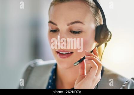 Veuillez maintenir la touche enfoncée pendant que je connecte votre appel. Photo d'une jeune femme attrayante portant un casque au bureau. Banque D'Images