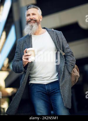 homme d'affaires confiant et mature marchant dans la rue de la ville, tenant un café dans un style de vie urbain Banque D'Images