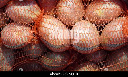 Tas de pommes de terre rouges crues dans un sac à ficelle rouge à vendre sur le marché de la ville locale. Banque D'Images